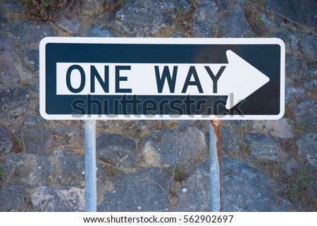 Concept One Way streetsign traffic direction with white right pointing arrow on black and dark wall as blurred background, copy space outdoor.