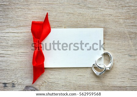 Valentine's day, empty white paper label, red ribbon, two silver hearts on wooden board