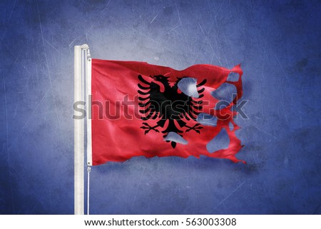 Torn flag of Albania flying against grunge background