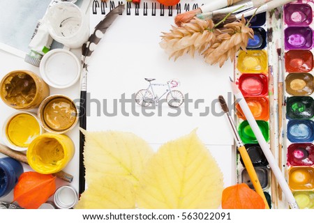 Pretty pictured bicycle on artist work flat lay. Top view on painter workplace with gouache and watercolor palette, paintbrushes and autumn yellow leaves. Fall inspiration concept