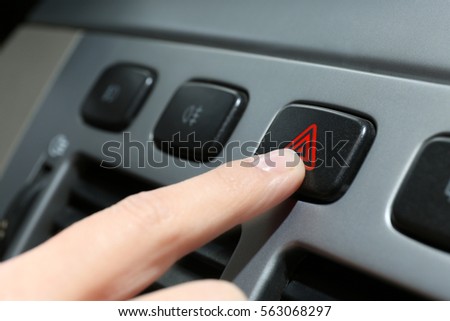 Male hand pressing emergency warning button on car console, closeup