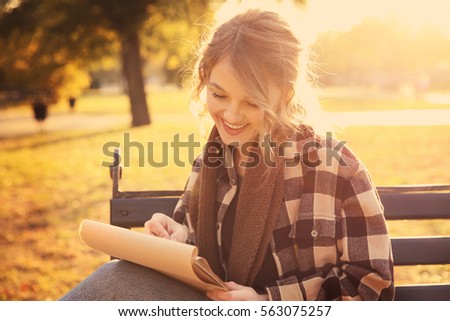 Young female artist drawing sketch while sitting on bench in beautiful park