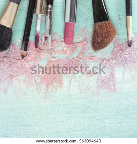 Makeup brushes and lipstick on a teal blue background, with traces of powder and blush on it. A square template for a makeup artist's business card or flyer design. With plenty of copyspace