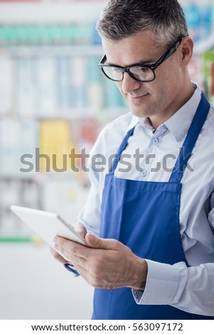 Professional supermarket clerk working with a digital tablet, he is searching products on the store shelf