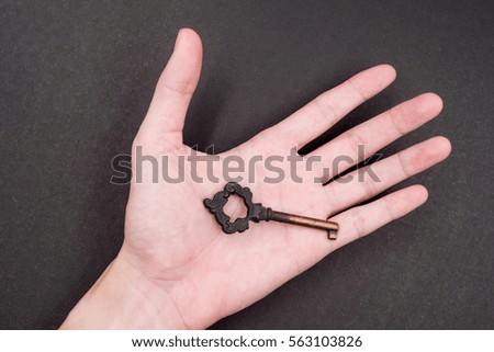 Male hand holding metal key on black background