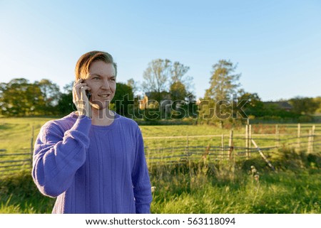 Young happy Caucasian man talking on mobile phone in peaceful grassy plain with nature