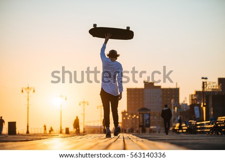 Young hipster man walking with longboard in hands on the boardwalk outside
