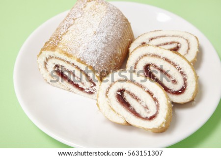 A strawberry jam Swiss roll cake on a pastel green background