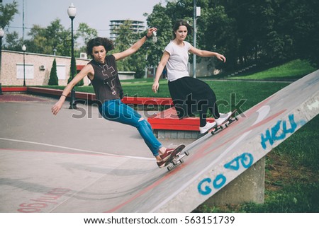 Two young girls enjoy skateboarding in the park in summer. Active live and sport concept. Toned picture