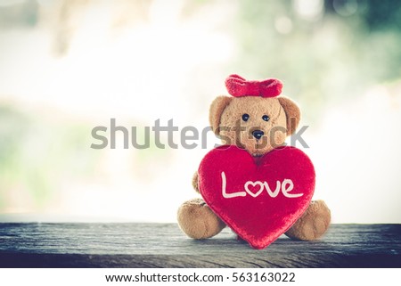 valentine day decoration with brown bear and red heart knitting shape on wooden mock up over blurred green garden on day noon light,Image for Happy Valentine holiday concept.