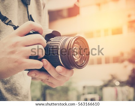 Photography or traveler Concept.The photographer hold DSRL camera in his hands with cityscape blur background and sunlight in summer time, selective focus. Photo of Vintage and filtered process. Royalty-Free Stock Photo #563166610