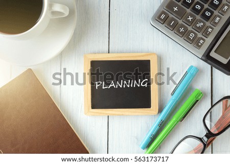 top view of PLANNING written on the chalkboard,business concept.chalkboard,notebook,calculator,pen,glasses,coffee on the wooden desk.
