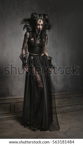 Young woman in black fantasy costume with feathers on dark background