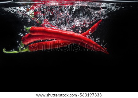 Red chili peppers falling into the water isolated on the black background