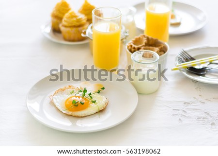 Traditional breakfast with fried egg, yogurt, homemade muffins, citrus curd and orange juice on white background. Selective focus. High key