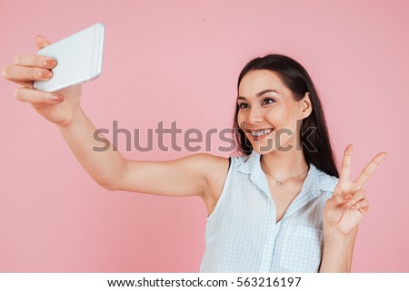 Portrait of a smiling cute woman making selfie photo on smartphone isolated on a pink background