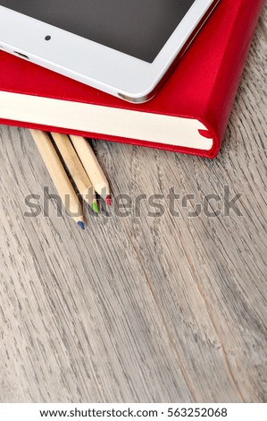 Red diary notebook, white tablet and colored pencils on desk wood texture
