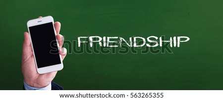 Smart phone in hand front of blackboard and written FRIENDSHIP