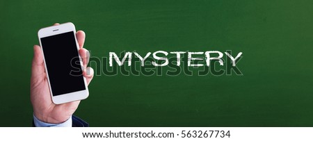 Smart phone in hand front of blackboard and written MYSTERY