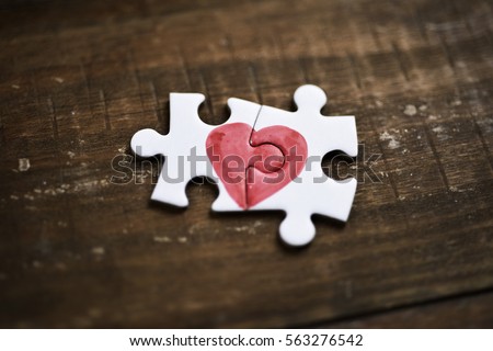 closeup of two pieces of a puzzle forming a heart on a rustic wooden surface, depicting the idea of that love is a thing of two Royalty-Free Stock Photo #563276542