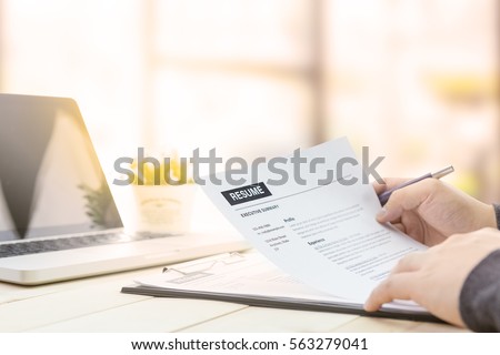Businessman review his resume on his wooden desk before sending to find a job with laptop computer, clock and glasses.