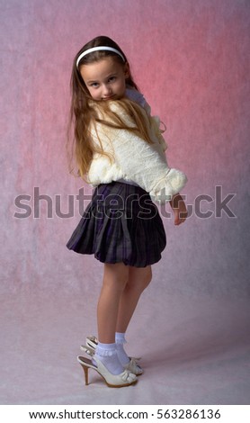 little girl trying on her mother's shoes on a pink background
