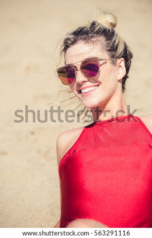 Young woman wearing sunglasses taking sunbath on a sandy beach. Vertical indoors shot. 