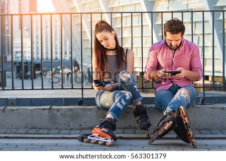 Couple with phones sitting. Inline skaters on urban background. Pay attention to your partner.