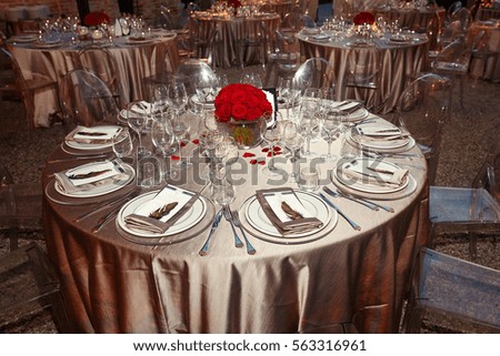 Round tables covered with silk cloth and decorated with red roses stand on backyard