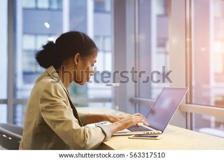 Young female business manager making marketing report for company using application on laptop computer with mock up screen connected to wireless network sitting near copy space for your advertising