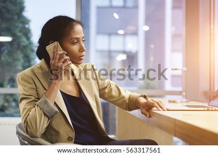 Professional female administrative manager talking on phone with employee giving advice and task for working day in office using laptop computer and wifi sitting near copy space for advertising