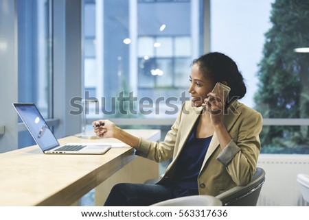Smiling female executive happy to sign successful contract with company while talking on cellular using laptop computer and wireless connection in office copy space area for your advertising content 