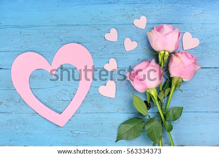 flowers (Roses) with colorful wooden hearts and paper heart on blue wooden background                               