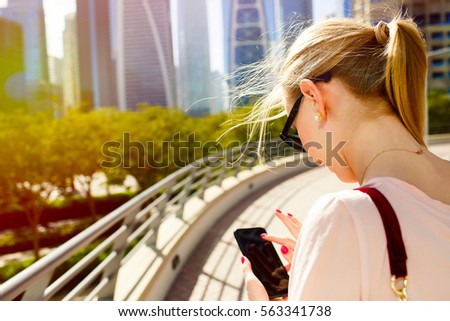 Blonde lady checks something in her iPhone standing on bridge before beautiful skyscrapers
