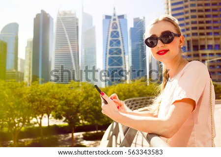 Smiling lady checks her iPhone standing on bridge before beautiful skyscrapers of Dubai