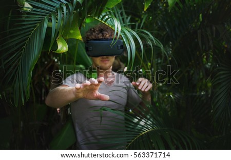 man in gray T-shirt, virtual reality 3D headset and exploring the play on a background of nature jungle