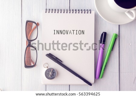 Top view of INNOVATION written on the note book.cup of coffee,glasses,compass,pen on the wooden desk