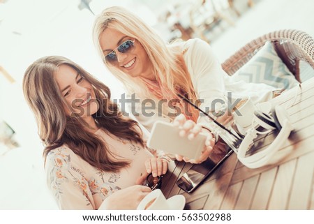 Two young women drinking coffee and using digital tablet in cafe