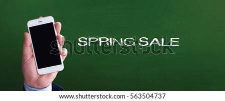 Smart phone in hand front of blackboard and written SPRING SALE