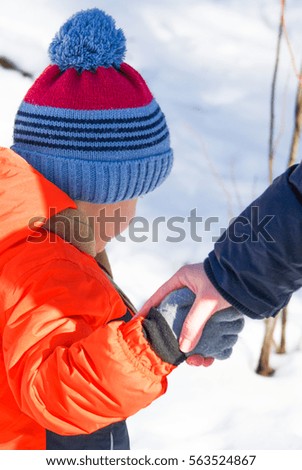 Beautiful young blonde mother walks hand and having fun playing with a little boy in the orange jacket on the background of winter snow in the park
