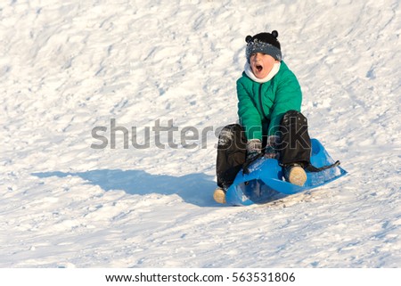 Boy playing in the snow. Sledding on a snowy hill. Winter games on snowy hill. Baby joy of snow. Throwing snowballs. Snow is the most fun for the kids. Winter holidays in the mountains.