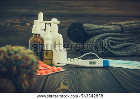 Medication tablets from illness and influenza on a rustic wooden background with woolen scarf and cap. thermometer with high temperature 39.1 per season, toned image
