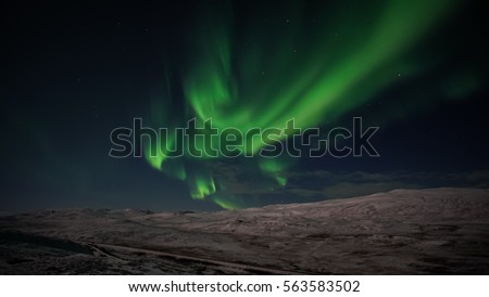 northern lights, aurora borealis above snowy hills and the lights of a car on the street down
