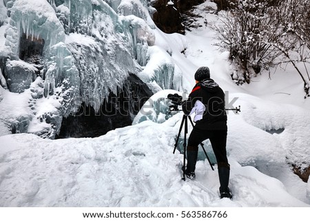 Professional landscape photographer taking picture and filming a frozen waterfall