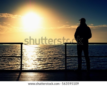 Adult tall man on pier board look over sea to morning Sun. Smooth water level in bay. Vivid and strong vignetting effect.