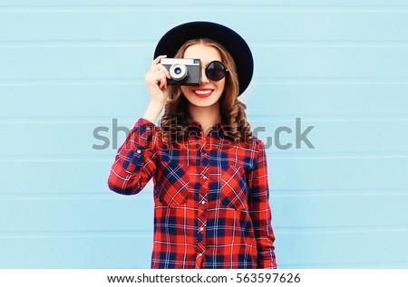 Portrait of happy smiling young woman photographer with film camera on blue background