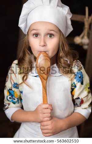 girl dressed cook stands with a large wooden spoon around the mouth