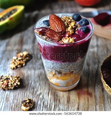 Overnight vanilla chia seeds pudding in almond milk and black sesame and beetroot dates smoothie, with fresh papaya, raw granola grains and seeds, dates, coconut crated, pomegranate and blueberries. 
 Royalty-Free Stock Photo #563614738