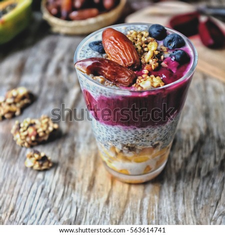 Overnight vanilla chia seeds pudding in almond milk and black sesame and beetroot dates smoothie, with fresh papaya, raw granola grains and seeds, dates, coconut crated, pomegranate and blueberries. 
 Royalty-Free Stock Photo #563614741