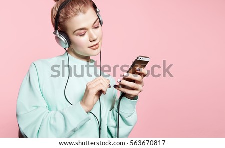 Beautiful young woman in headphones listening to music smiling with closed eyes standing on a pink background in a blue sweatshirt Royalty-Free Stock Photo #563670817